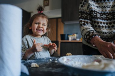 Neşeli torun, mutlu büyükanneye mutfakta pasta pişirmesinde yardım ediyor. Yüzünde un olan komik kız aile yemeği için tatlı pişirmesine yardım ediyor.