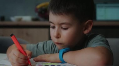 Yürümeye başlayan bir çocuk elinde kırmızı bir işaret ve çizim ile bir masada mutlu bir şekilde oturur. Elleri ödevine odaklanırken hareketler yapıyor, arsız gülen yüzler yaratıyor.