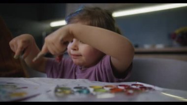 Küstah bir çocuk, mutlu bir şekilde resim yapar. Kaşları konsantrasyon içinde yükseldi, yüzünde mutlu bir ifade var, neşesini jestlerle paylaşıyor ve...