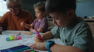 Çocuklar ve bir kadın iç açıcı bir videoda resim çiziyorlar. Kadınlar desteklerken çocuklar sanat eserleri yapıyor. Güçlü aile bağları, yaratıcı aktivitelerden hoşlandıkları kadar bariz.