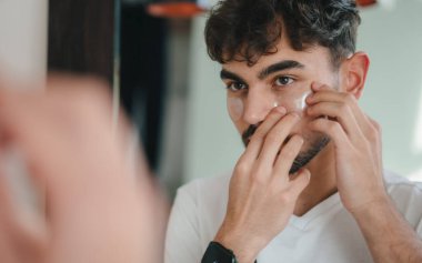 Mutlu adam aynaya bakıyor, banyoda göz bandı yapıştırıyor. Evde yalnız zaman geçirmek, cilt bakımı, ev hayatı ve yaşam tarzı konsepti..