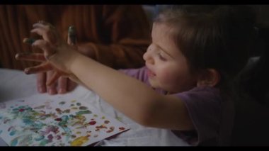 Genç bir kız babasının gözetiminde canlı ve kaotik bir parmak boyamasına katılıyor.
