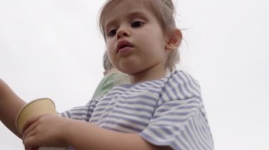 Tatlı bir çocuk elinde bir dondurma bardağı tutuyor, mutlu bir şekilde gülümsüyor ve güneşli bir günde dışarıda eğleniyor.