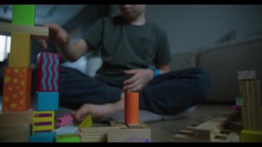 Genç bir çocuk, konsantrasyon ve yaratıcılık gösteren, rahat bir oturma odasında renkli bir blok kulesi inşa ediyor..