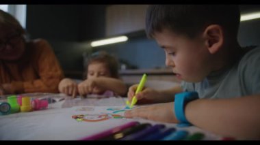 Çocuklar bir masadaki kalemlerle çizim yapıyor, yaratıcılığı vurguluyor ve bir sınıfa veya ev ortamına odaklanıyor.