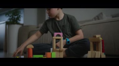 Genç bir çocuk, sıcak ve davetkar bir oturma odasında canlı ahşap bloklarla oynayıp inşa ediyor.