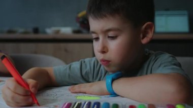 Genç bir çocuk, bir çizimi kırmızı bir kalemle boyamakla meşgul, yaratıcılığını ve dikkatini gösteriyor.