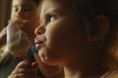 Çocuklar çubuklarda renkli dondurmanın tadını çıkararak yaz neşesinin ve hazzının özünü yakalıyorlar.