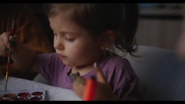 A young girl is joyfully exploring her creativity through paints and various crafts, enjoying every moment