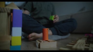 Genç bir çocuk neşe içinde yaratıcı bir oyun oynar. Renkli ve canlı yapı taşları zemine yayılır.