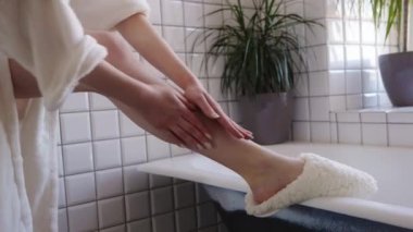 Huzurlu bir spa sahnesi, rahat terliklerle, rahatlatıcı ve sakin bir şekilde losyon süren birini gösterir.