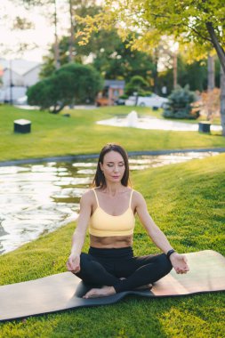 Bir kadın gün batımında huzurlu ve sakin bir ortamda minderinde yoga meditasyonu yapıyor.