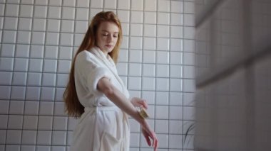 Genç bir kadın, cilt bakım ürünlerini huzurlu bir ortamda uygularken gerçekten huzurlu bir spa anının tadını çıkarıyor.