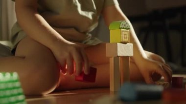 Çok genç bir çocuk ahşap zeminde renkli ve canlı bloklar yığarak yaratıcı oyunlara girişiyor.