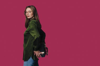 Yeşil bluzlu şık bir kadın canlı pembe bir arkaplanda duran el çantasıyla poz verir..