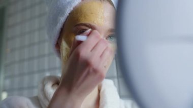 Bir kadın şık banyosunda lüks altın bir maske takıyor ve özen gösterme alışkanlıklarını benimsiyor.