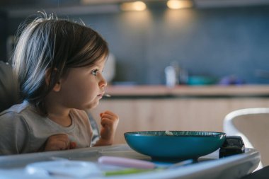 Meraklı ve neşe dolu küçük bir çocuk mutfak masasında oturur ve lezzetli bir kahvaltı yapar.