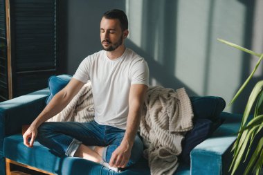 Huzurlu bir ortamda, bir adam farkındalığa dalıyor, rahat mavi bir kanepede sessizce meditasyon yapıyor, tamamen mevcut.