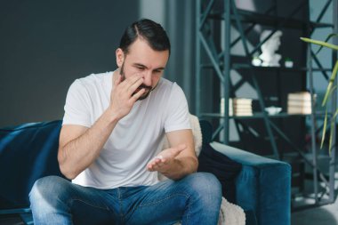 Bir adam şık bir ev ortamında otururken akıllı telefonunu kontrol ederken artan hayal kırıklığını gösterir.