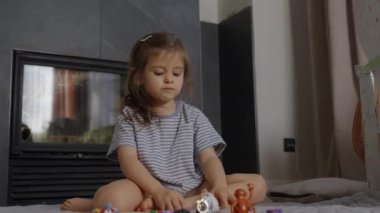 Genç bir kız sıcak bir salondaki oyun aktivitelerine odaklanmış bir şekilde yerde oturuyor.