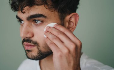 Genç bir adam titiz bir şekilde pamuk pedi kullanarak cilt bakımı yapıyor.