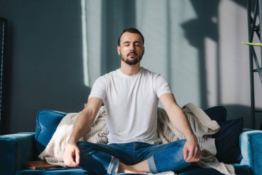 Genç bir adam kanepede huzur içinde meditasyon yapar. Şık, modern bir tasarım ve konfor evinde huzur saçar.