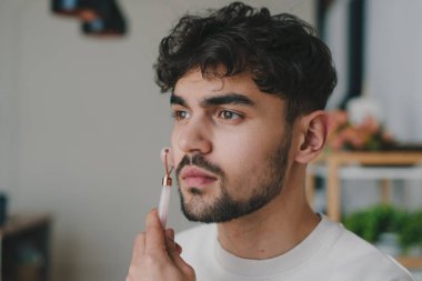 Modern dekorlar ve rahatlatıcı titreşimler arasında, evde cilt rutinine konsantre olan şık bir genç adam.