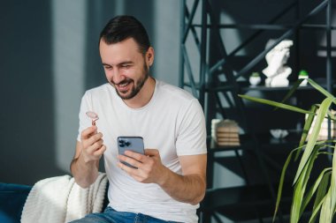 Neşeli bir adam şık ve çağdaş bir odada yüz silindiri tutarken akıllı telefonuyla meşgul olur.