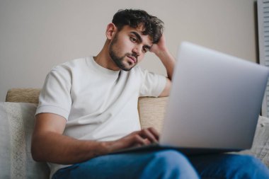 Dizüstü bilgisayarı üzerinde çalışan odaklanmış genç bir adam, ev hayatı tarzından modern bir çalışma sergiliyor.