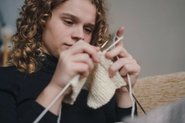 Rahat, sıcak ve rahat bir ortamda, genç bir insan özenle yumuşak ve davetkar bir kumaş örüyor.