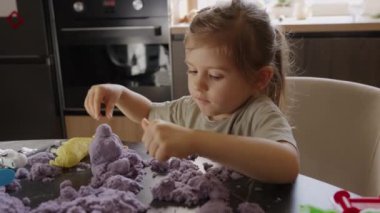 Bir çocuk mor kinetik kumla neşeyle oynar, oyun sırasında yaratıcılığı ve motor becerileri artırır.