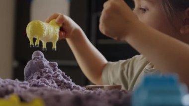 Bir çocuk mor kinetik kumla ve sarı oyuncak ördekle meşgul olur, yaratıcılığı ve hayal gücünü teşvik eder..