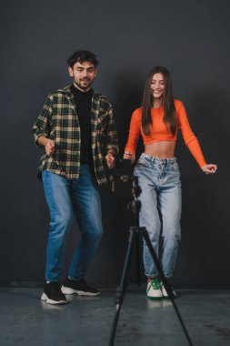 İki enerjik ve neşeli kişi, arkalarında karanlık bir zemin olan bir stüdyoda coşkuyla dans ediyorlar.