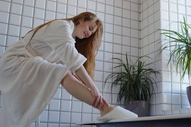 Hoş ve sakin bir sahne, rahat bir bornoz içindeki bir kadını modern bir banyo ortamında esneyerek resmediyor.