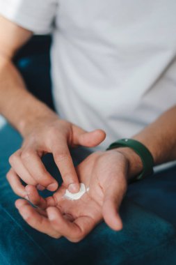 Günlük cilt bakımının bir parçası olarak ellerine nemlendirici krem süren bir birey.