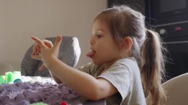 Genç bir kız renkli kinetik kumla karmaşık şekiller yapmaya odaklanır ve yaratıcılığını gösterir.