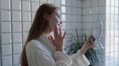 Genç bir kadın rahat bir banyoda cilt bakım ve refahını arttırmak için cilt ürünlerini inceliyor.