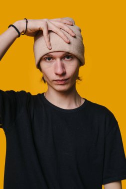 Şık bir genç adam, modaya uygun bir bereyle canlı sarı bir arkaplan karşısında, modern modaya uygun poz veriyor.