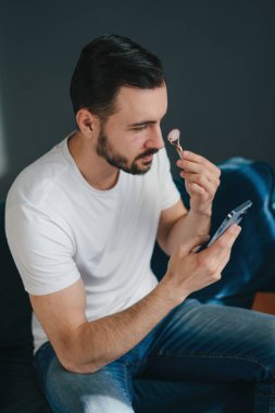 Bir adam aynanın karşısında cilt bakımını takip eder, özen göstermenin ve tımar etmenin önemini vurgular.