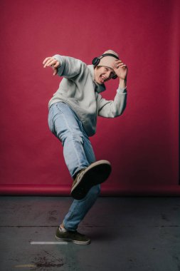 Tarz sahibi gri kapüşonlu bir genç enerjik bir şekilde kulaklık takarken dans pozu veriyor.
