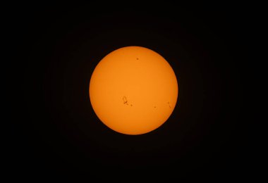 Turuncu renkli öğleden sonra güneşi, siyah bir zemin üzerinde ev yapımı güneş filtresi kullanarak birçok güneş lekesi ile parlıyordu..