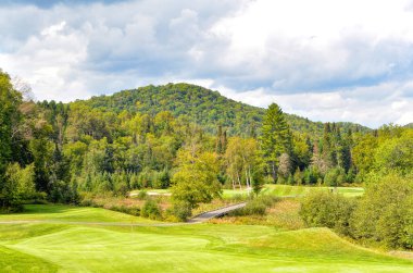 Kanada 'da güzel bir yaz gününde bulutlu gökyüzü ile yuvarlanan tepelerin arasında yeşil bir golf sahası