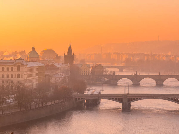 Winter frosty dawn over Prague. Picturesque golden glow and winter haze over Vltava river with bridge and historic town around. Prague, Czech Republic