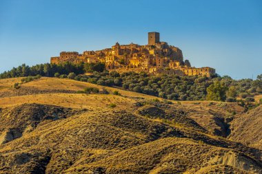 Kum taşından yapılmış terk edilmiş, eski bir dağ kasabası olan Craco 'nun pitoresk bir manzarası. Craco, 20. yüzyılın sonlarında meydana gelen deprem yüzünden terk edilmiş bir hayalet kasaba. Matera ili, Basilicata, İtalya