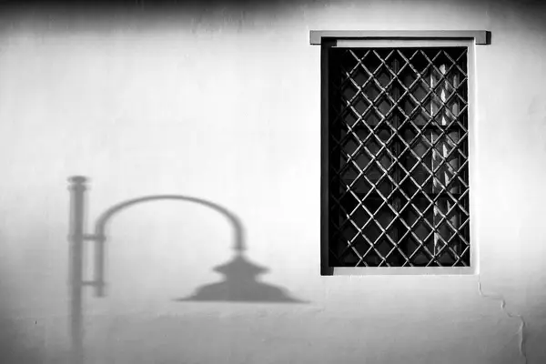 stock image  Black and white photograph of a window with lattice bars and the shadow of a vintage lamp post on a white wall