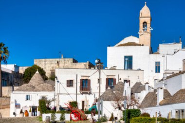 İtalya 'nın Alberobello kentindeki Via Indipendenza boyunca Chiesetta Rettoria SS' in çan kulesiyle Trulli evleri görülüyor. Arka planda Sacramento ve S. Lucia var..