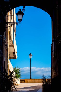 Via Venezia, Bari, İtalya 'da bir kemer tarafından çerçevelenmiş, parlak mavi gökyüzü ve arka planda bulutlar olan bir lamba manzarası