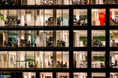 Modern bir ofis binasının dış cephesi gece aydınlanır, mimari tasarımı ve ışıklandırması sergilenir..