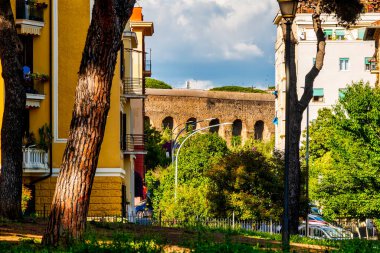 Villa Fiorelli Parkı, Roma, İtalya 'daki ağaçlar ve binalar tarafından çerçevelenmiş Acquedotto Felice manzarası
