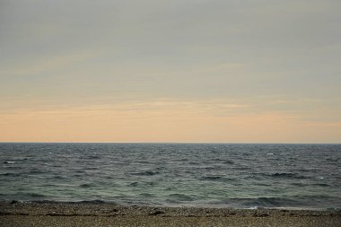 Önünde kumsal olan ufukta gökyüzü sarı ve mavidir. Deniz neredeyse sakin..